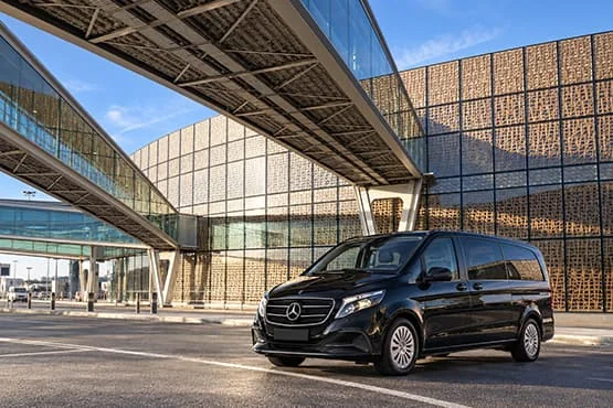 Van Mercedes noir devant un bâtiment moderne et des passerelles vitrées.