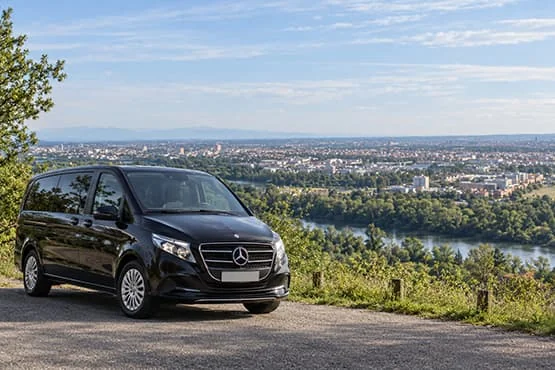 Van Mercedes noir devant un panorama urbain traversé par un fleuve.